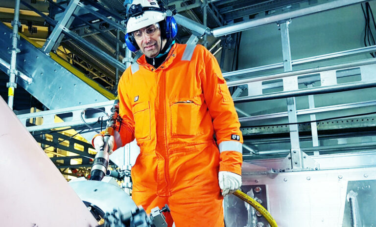 a man in an orange coverall standing next to a machine.