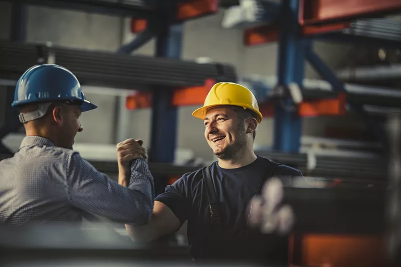 two men in hard hats are shaking hands.