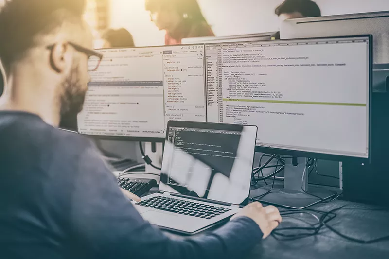 a man sitting in front of two computer monitors.