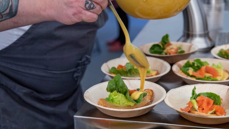 a person pouring dressing onto small bowls of food.