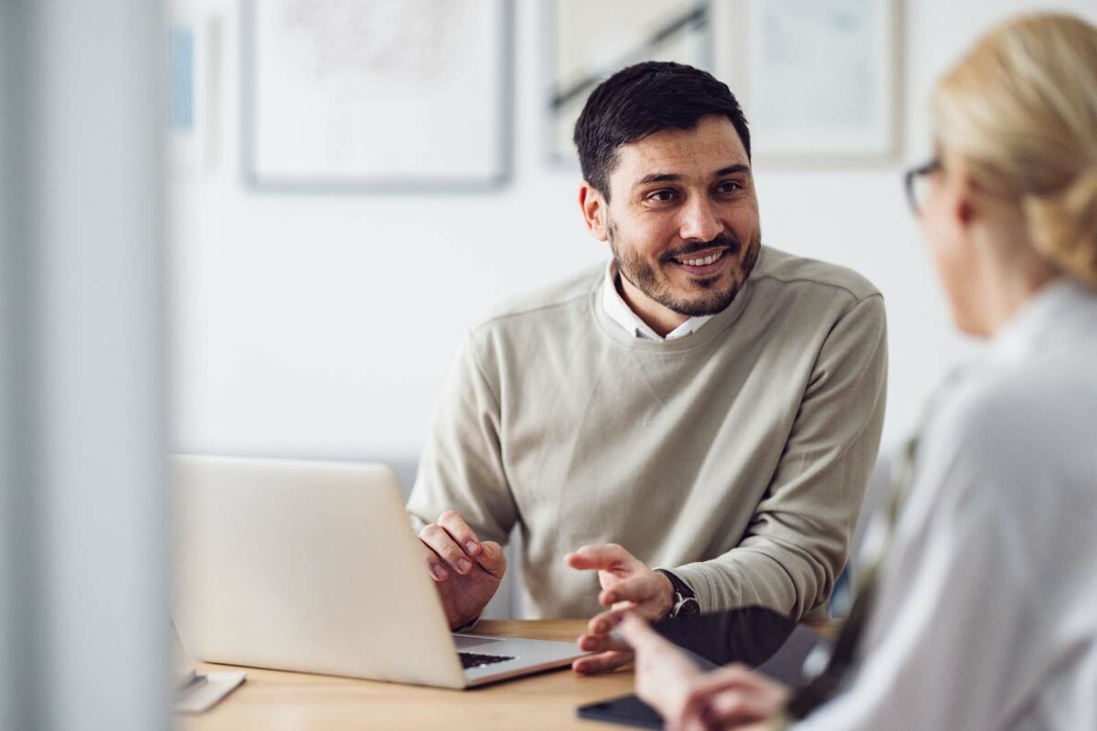 a man talking to a woman in front of a laptop.