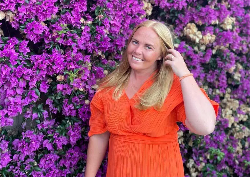 a woman in an orange dress standing in front of purple flowers.